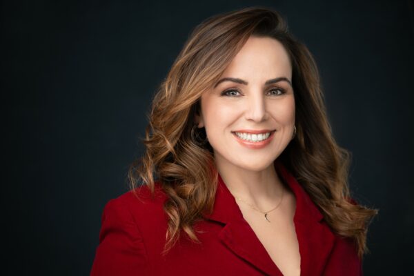 A picture of a smiling woman with light skin and brown hair wearing a red blazer