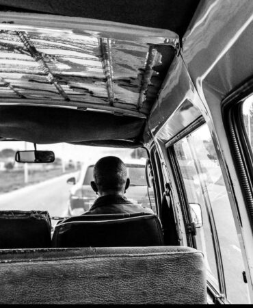 An image of the back of someones head sitting on the right seat of a car.