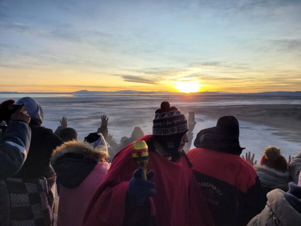 Several individuals stand on top of Llipi Mountain as the sun rises