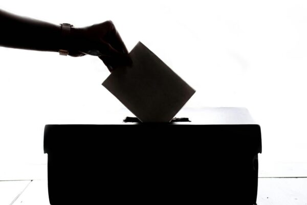 silhouette of a person's hand placing a ballot into a ballot box