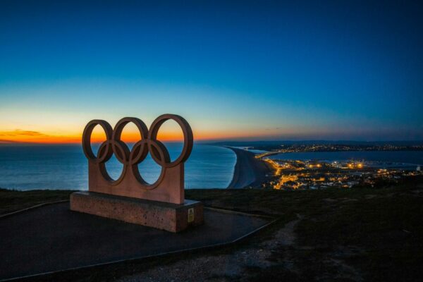 statue of Olympic rings overlooking a shore town and sea